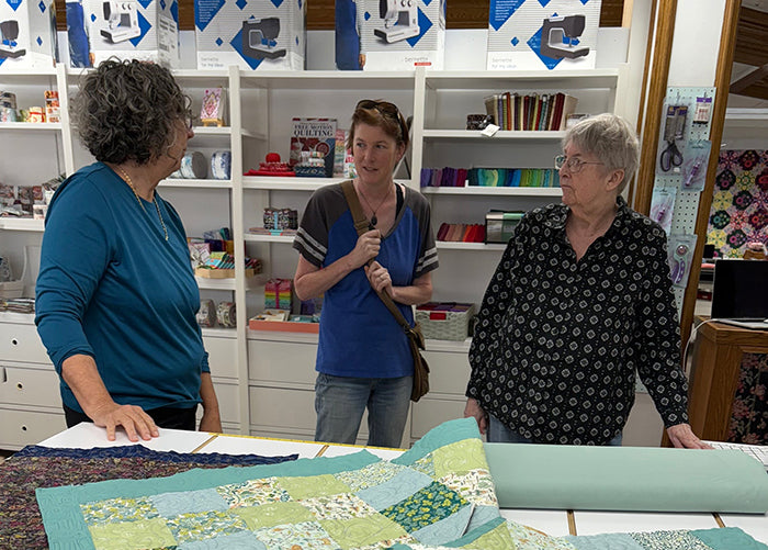 Three people in a room with a large quilt on a table