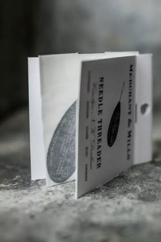 Booklet titled 'Needle Threader' on a textured surface with a blurred background
