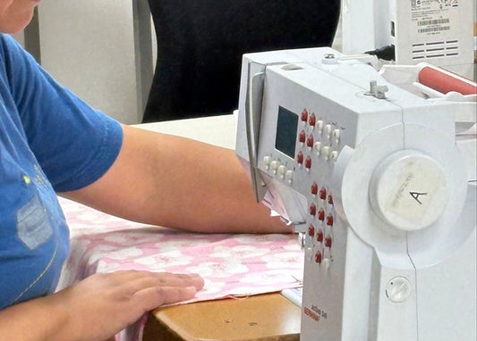 Person operating a sewing machine with a focus on the machine's controls and the fabric being sewn.